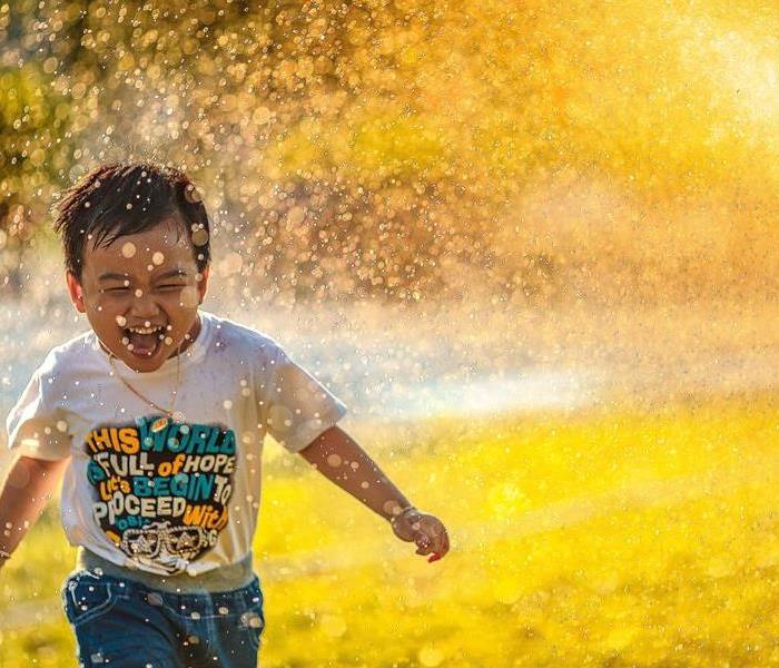 A happy child runs through a sprinkler's stream of water