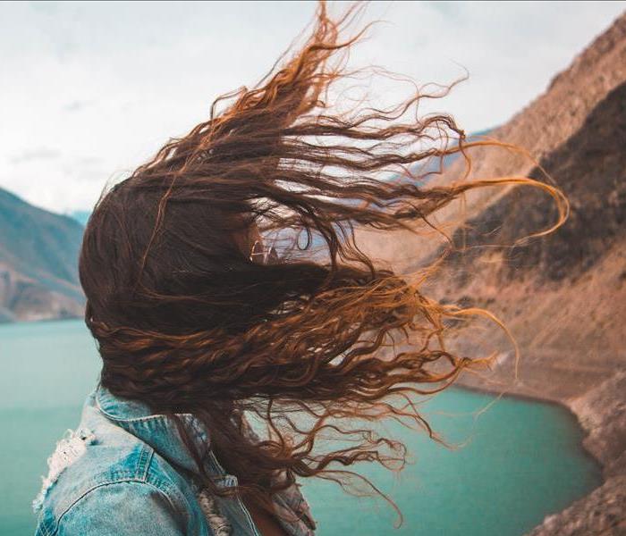 A woman's hair is blown in the wind in front of a lake