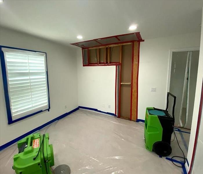empty white room with a wall cut out due to water damage with 2 green dehus in the room 
