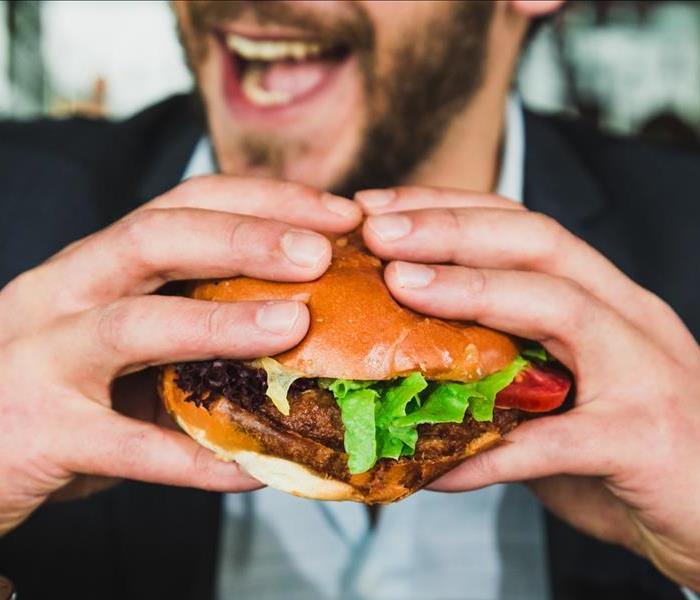 A man in a business suit holds a hamburger