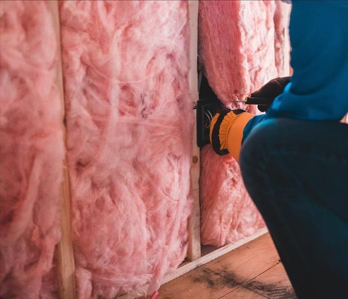 A man in a dark attic looks at pink insulation.