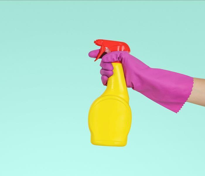 A pink gloved hand holds a yellow bottle